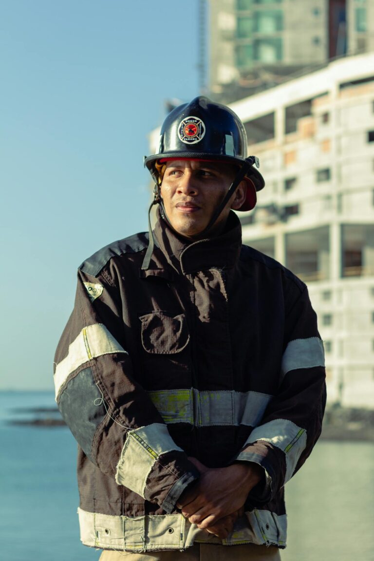 A firefighter in full gear stands confidently near a waterfront construction site.